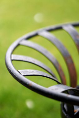 A vertical closeup detail of an old rusty metal bench on a blurred green background
