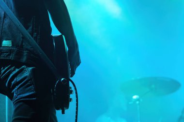 Man playing electrical guitar during concert. Detail on hand and guitar. Blue light in background with a lot of negative space