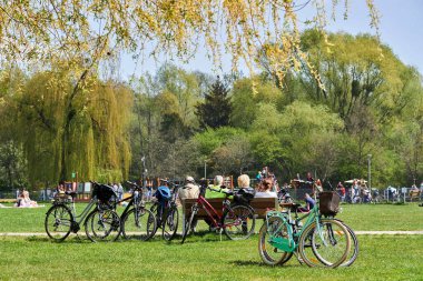 The people resting near bicycles parked on green grass by the Rusalka lake on a sunny spring day