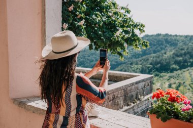 A view of a Caucasian female photographing a forest from a balcony