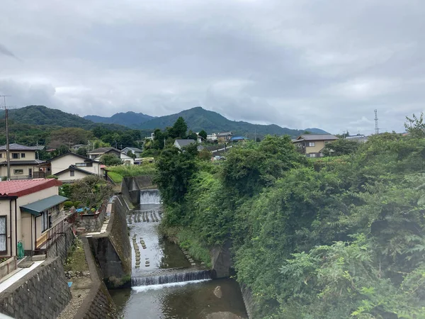 A river flowing between houses and trees with mountains in the background