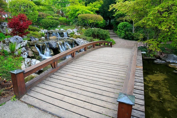 A small bridge above a river surrounded with greenery in a Japanese garden