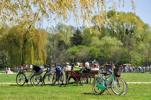 The people resting near bicycles parked on green grass by the Rusalka lake on a sunny spring day