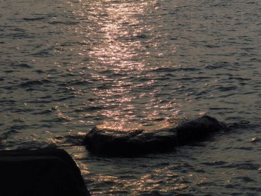 A beautiful view of rocks in the sea with the reflection of sunset sky