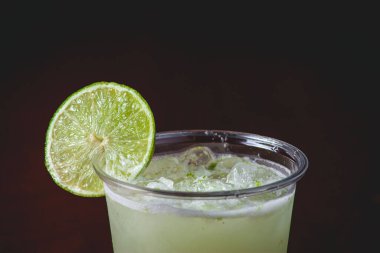 A closeup of a glass of icy mojito cocktail with a slice of lime on a dark background