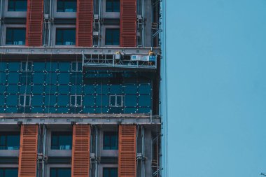 A couple of working building window cleaners on a platform against a clear sky