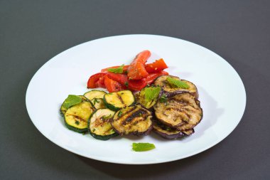 grilled peppers, zucchini and eggplant on white plate on dark background. typical Italian vegetarian antipasti
