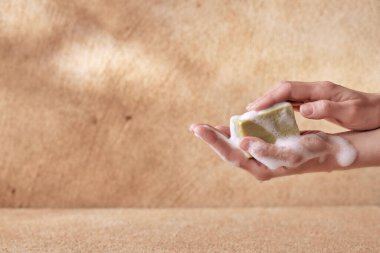 A young woman touching a foamy soap with her hands on a beige background for spa advertising
