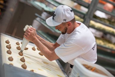 A male confectioner preparing cookies on a tray using a forcing bag