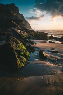 A vertical view of a beautiful rocky beach during a scenic sunset