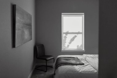 A grayscale of a bed and a chair in a bedroom with a window