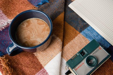 A top view of coffee, vintage camera, and notebook on a blanket