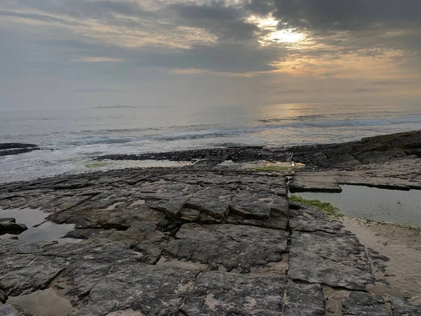 A natural landscape with a flat rocky shore and sun bean through the clouds at sunset of sunrise