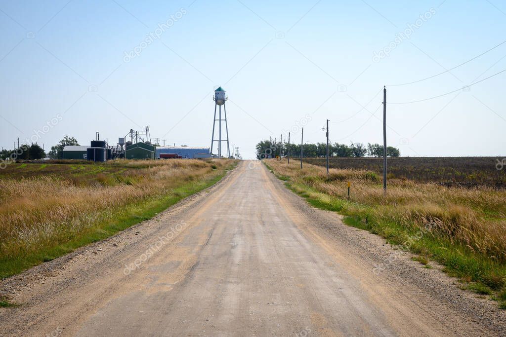 A dirt road surrounded by green fields and rural houses on a sunny day in Kansas, USA