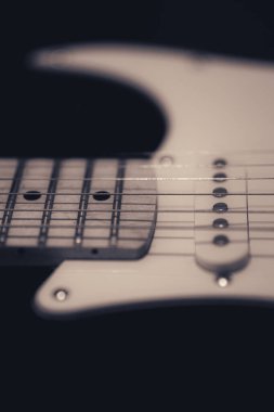 A vertical closeup of white electric guitar in the dark