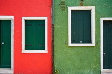 A scenic view of red and green buildings with wooden windows in Burano, Venice, Italy