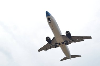 A low angle shot of a white passenger airplane flying against a cloudy sky