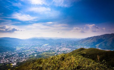 Dağ sıralarının güzel manzarası ve altında bulutlu gökyüzü olan bir kasaba.