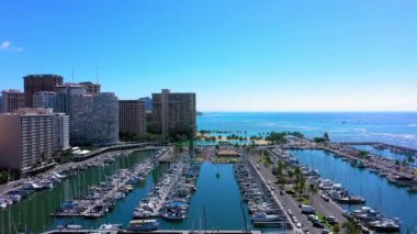 A drone shot over a harbor full of boats with the city's buildings on the side in Waikiki, Hawaii
