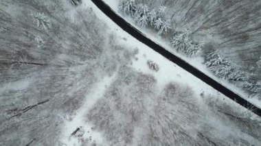 An aerial shot of a road surrounded by leafless forests covered with snow in winter in Bavaria,Germany