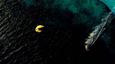 An aerial drone shot of a kite surfer surfing on the calm waters of the ocean