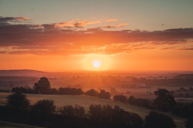 A beautiful view of a sunset in a cloudy sky above a field with trees
