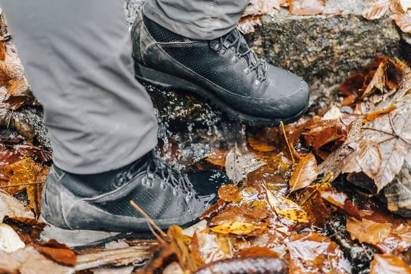 Close up detail photo of hiking or trekking boots in muddy autumn trail. Mountain leather shoes on dirty terrain, wet ground and stepping into water.