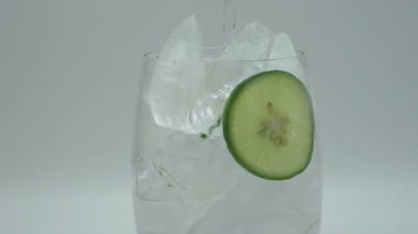 A closeup shot of water pouring in a glass ice cup with lemon slices on isolated background