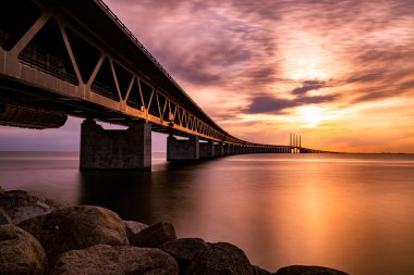 A low angle shot of a bridge over the sea on a golden sunset sky background