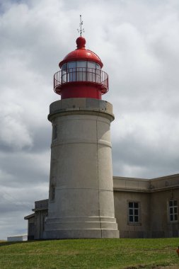 A vertical shot of The Ponta do Albernaz Lighthouse (Farol de Albarnaz) against cloudy sky in bright sunlight in Flores Island, Azores, Portugal