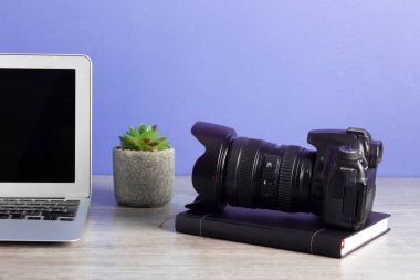 Kameralı, dizüstü bilgisayarlı, ahşap masada saksı bitkisi olan fotoğrafçı.