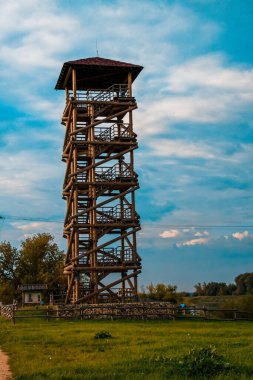 A vertical shot of a tall wooden tower in the countryside surrounded by a lush green field