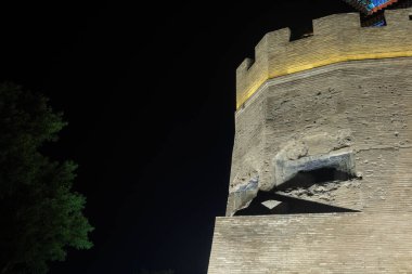 A part of a medieval fortress with half-destroyed windows illuminated at night against the dark sky