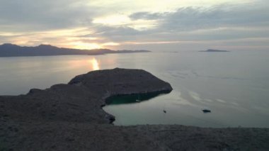 An aerial view of the wavy sea and the rocky mountains gleaming under the cloudy sunny sky in 4K