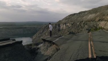 A cool young skater boy standing on the edge of a broken rural road