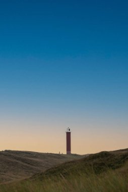 A vertical shot of a lighthouse on a coastal hill against a clear sky background