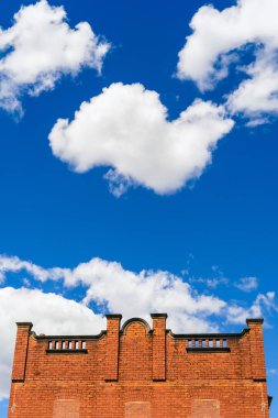 A vertical low angle shot of a brick architecture building against a blue sky with cumulus clouds