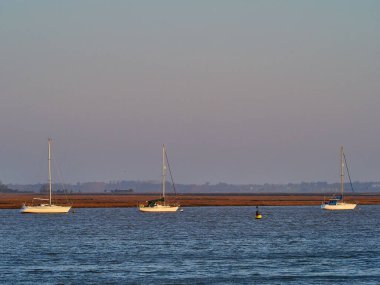 Three boats sailing on the backwater at Walton-on-the-Naze, Essex, over a background of the sky colored by the sunrise