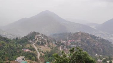 An aerial shot of houses on the Uttarakhand Mountains range, trees and foggy mountains in India