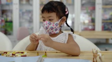 An adorable Thai female child in a patterned mask playing with toys