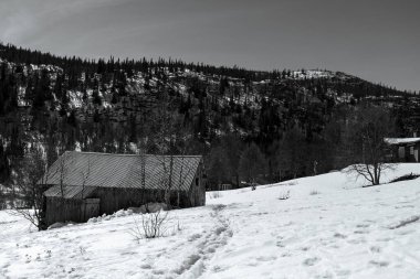 A grayscale shot of a small house on a snow-covered hilltop