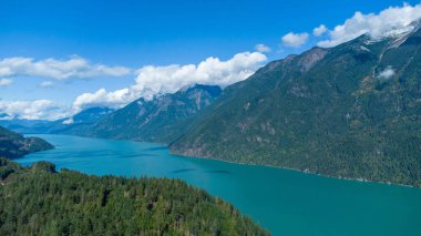 A beautiful view of a calm lake surrounded by dense trees and mountains