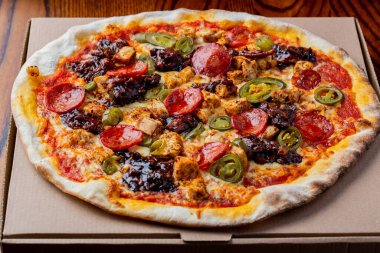 A close-up shot of a freshly baked pizza with salami, and jalapeno peppers.