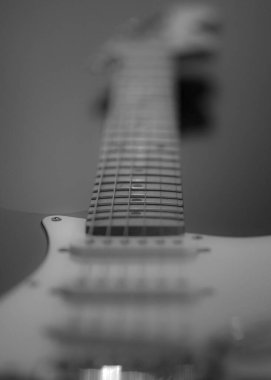 A low angle selective focus shot of the neck of white electric guitar in the dark
