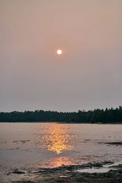 A vertical shot of the red sun of the evening is reflected in the waters of the lake