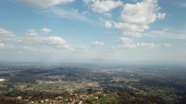 A drone view of the city landscape, city surrounded by green hills, trees under a blue cloudy sky