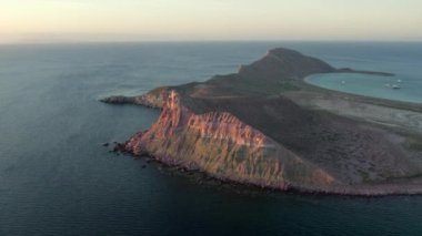An aerial view of the wavy sea and the rocky mountains gleaming under the cloudy sky in 4K