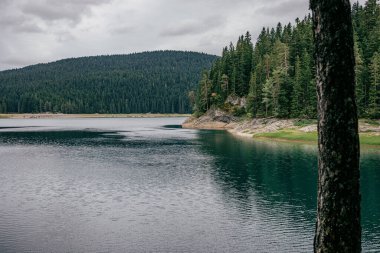 A gloomy summer day in the countryside of Montenegro with a clear lake surrounded by lush greenery