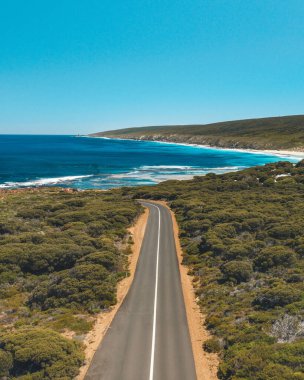Denize giden yemyeşil bir doğayla çevrili bir yolun dikey görüntüsü.