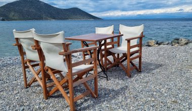 A wooden table and white chairs on a beach in Greece